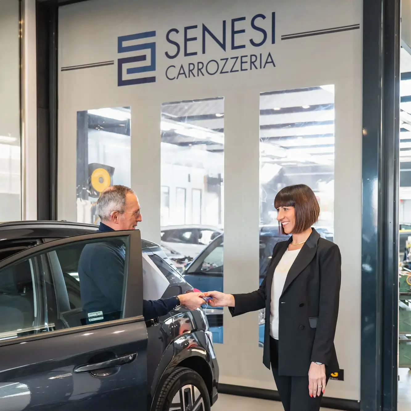 Il proprietario della Carrozzeria SENESI consegna le chiavi di un'auto riparata a un cliente soddisfatto.